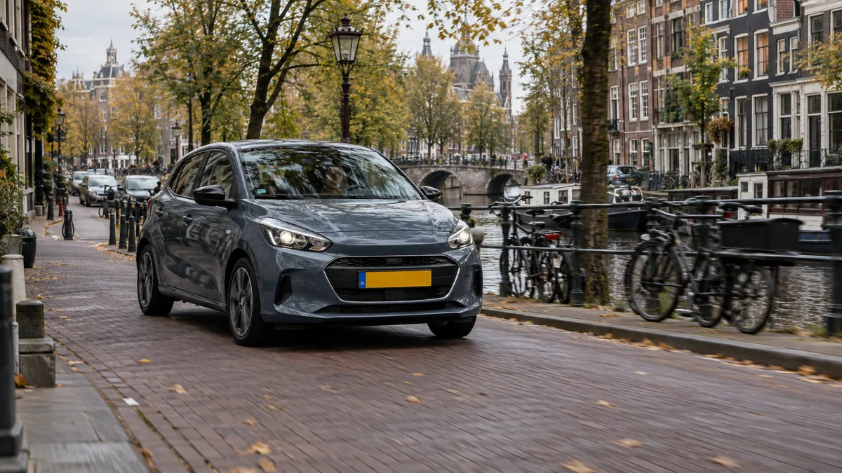 Compacte hatchback stadsauto rijdt door een Amsterdamse grachtenstraat met grachtenpanden en fietsen